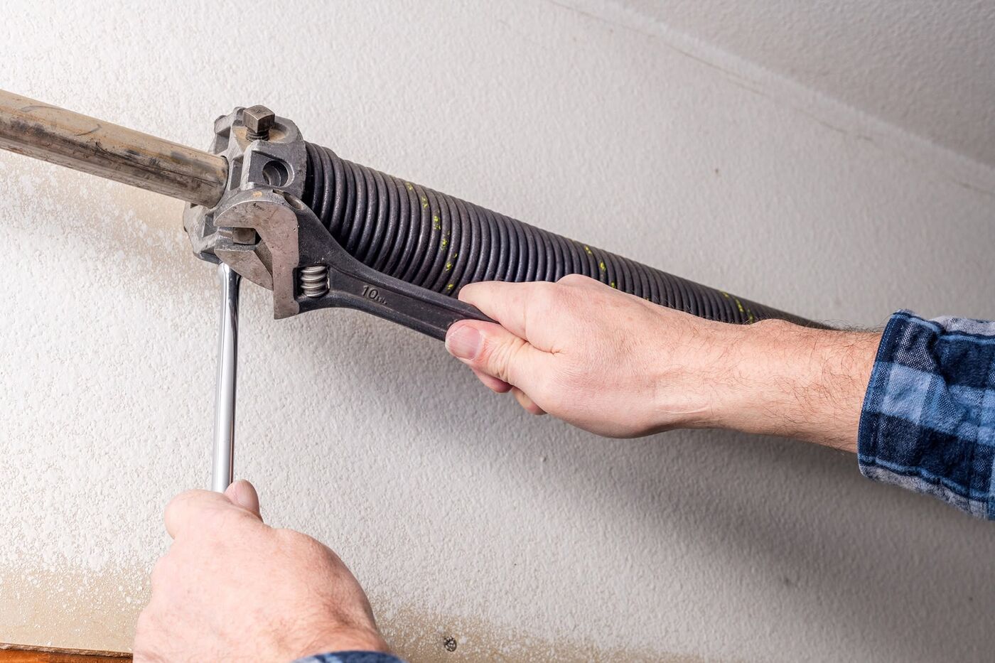 Technician using a winding bar and wrench to safely tension a garage door torsion spring
